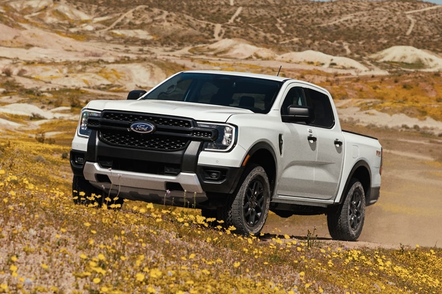 A 2024 Ford Ranger® in Oxford White is being driven up a sandy hill in a scenic location