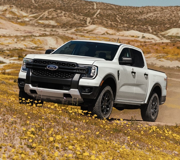 A 2024 Ford Ranger® XL in Oxford White is being driven on a dirt road in a scenic location