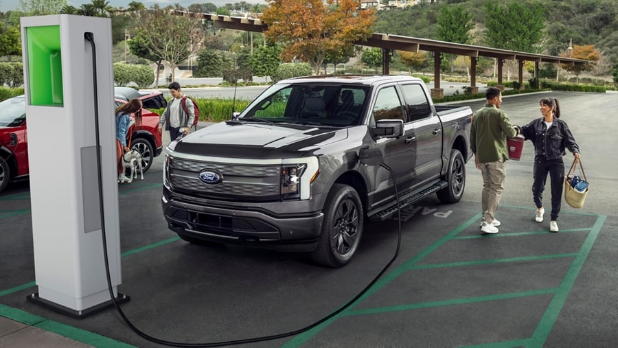 A 2023 Ford F-150® Lightning® plugged in at public charging location. A man and a woman converse outside the truck