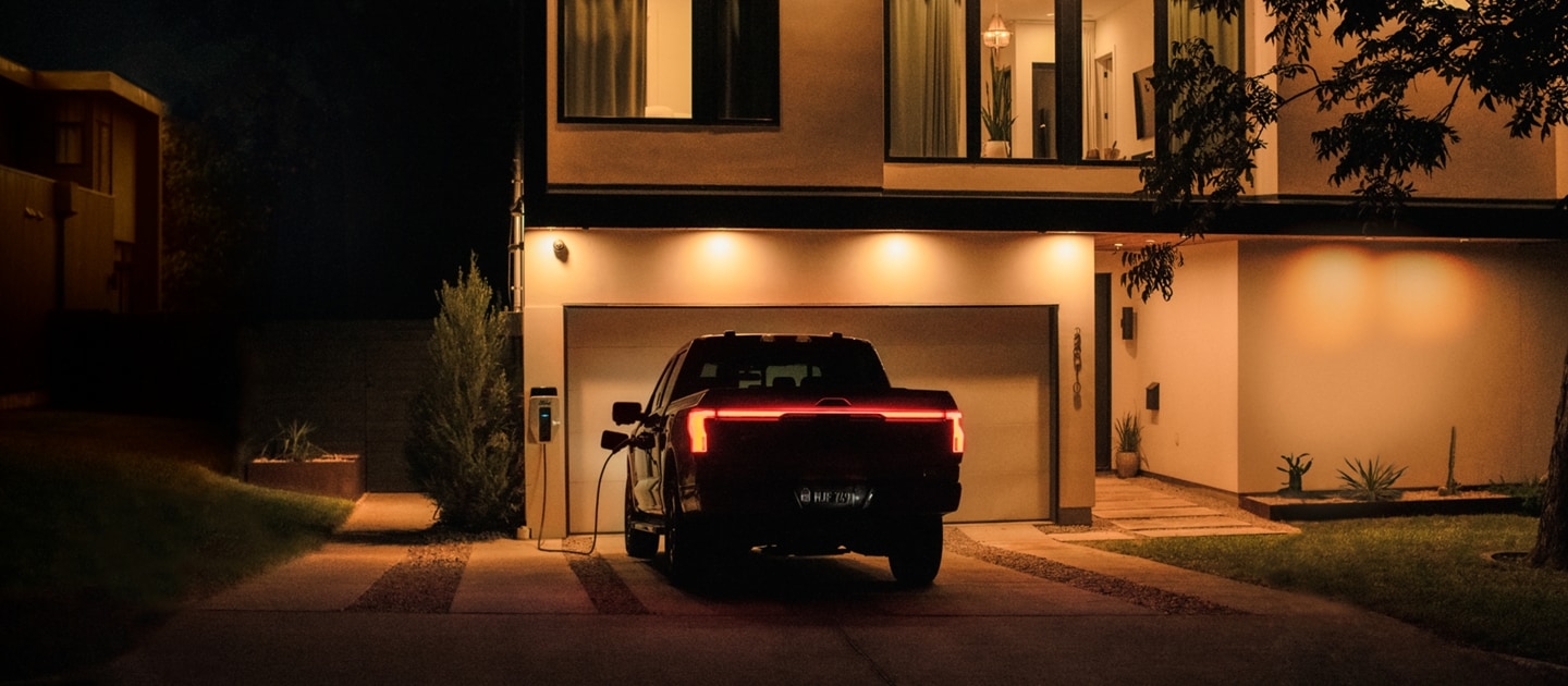 A 2023 Ford F-150® Lightning® parked in a house's driveway at night. The house lights are on because of Intelligent Backup Power