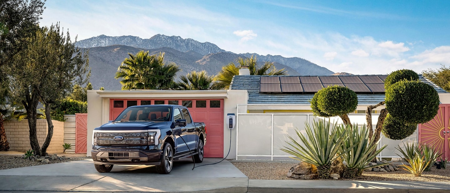 A black 2023 Ford F-150® Lightning® backed into the driveway of a suburban home. The landscape feels arid, almost desert like