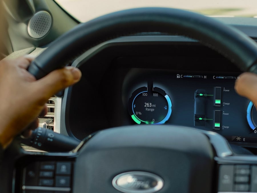 Steering wheel of a 2023 Ford F-150® Lightning®, gripped by a driver's hands. On the instrument cluster, a battery level indicator