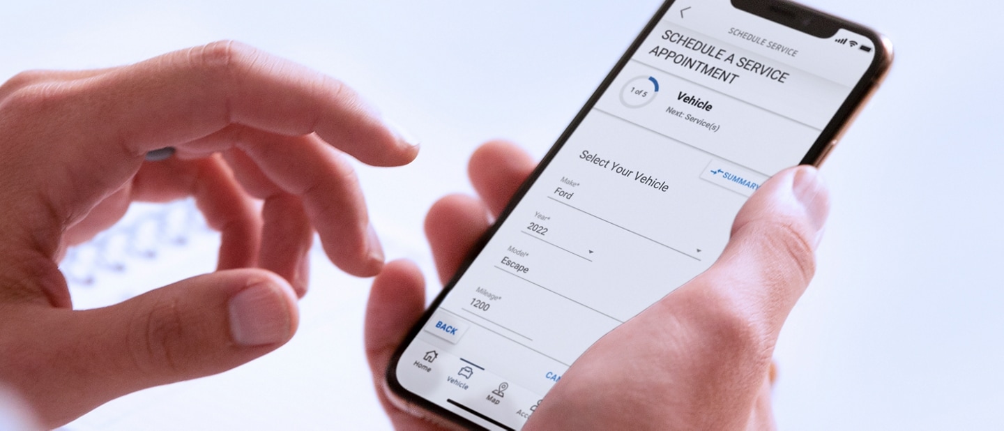 A hand holds a smartphone displaying the Schedule Service menu in the FordPass™ App