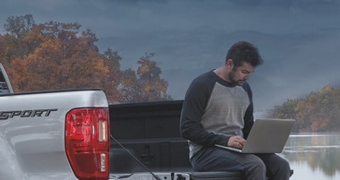Man using laptop while sitting on truck bed of 2020 Ford Ranger Lariat parked near lake