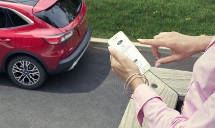 Woman standing on a balcony holding a mobile phone with 2021 Ford Escape in the background  