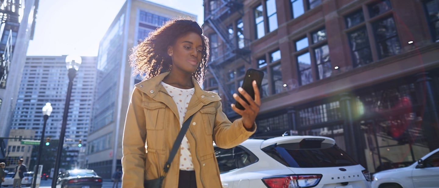 Woman walks on city sidewalk and uses her smartphone