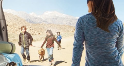 Woman sitting in open rear of a Ford Explorer while family and dog walk in desert in the distance